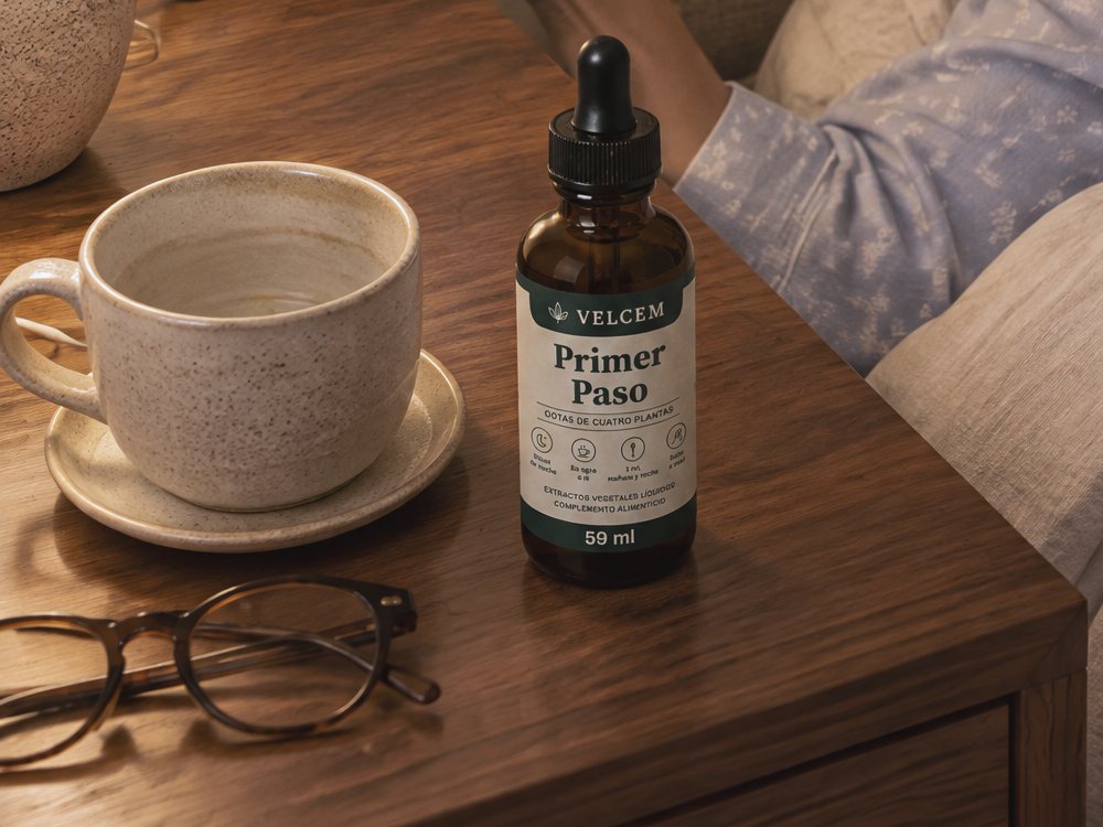 La mesilla de noche con la taza vacía, el frasco de VELCEM Gotas Primer Paso y las gafas de leer